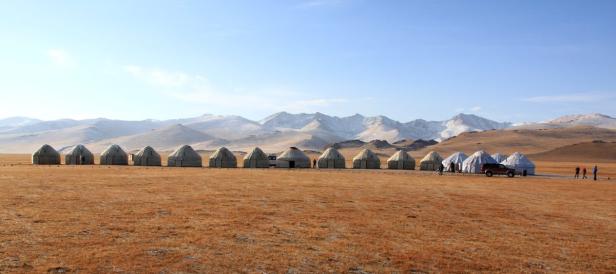 Eine Reihe von Jurten in einer weiten Landschaft mit schneebedeckten Bergen im Hintergrund.