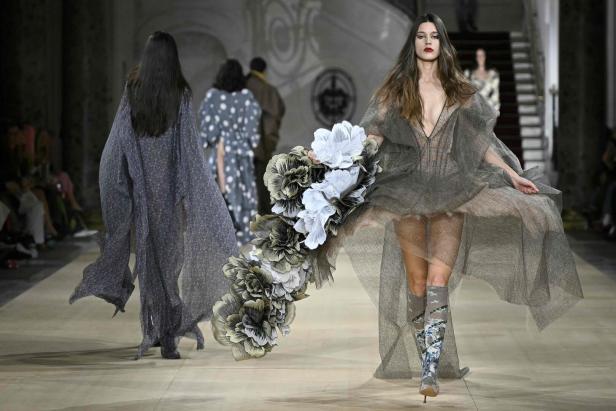 Eine Frau in einem transparenten Kleid mit Blumen auf einem Laufsteg.
