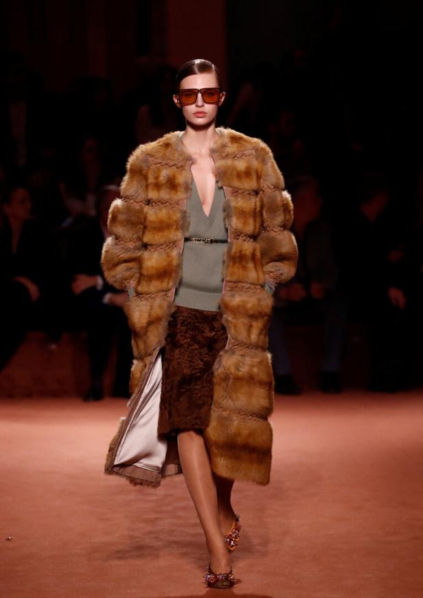 Eine Frau auf dem Laufsteg trägt einen braunen Pelzmantel und orangefarbene Sonnenbrille.