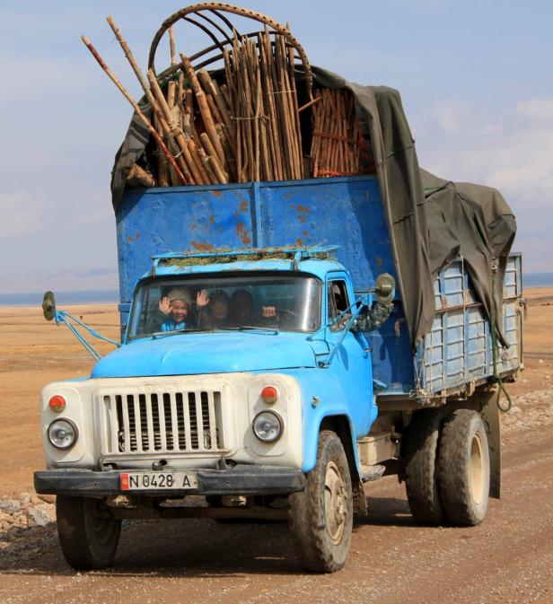 Ein blauer Lastwagen transportiert Holz und andere Materialien durch eine ländliche Gegend.