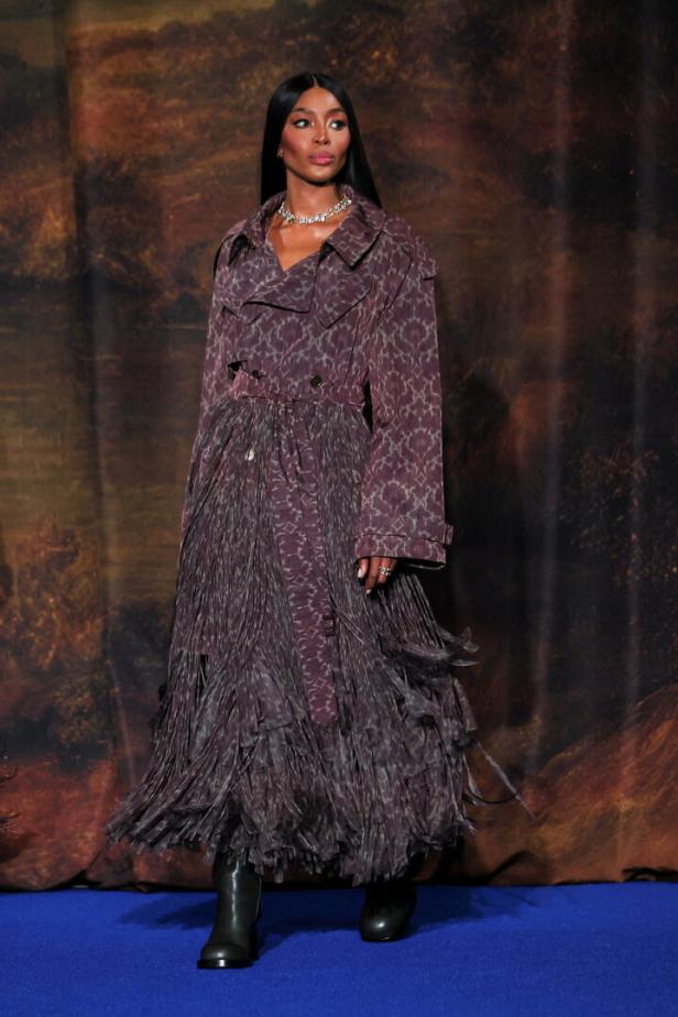 Naomi Campbell trägt einen gemusterten Mantel mit Fransen und Stiefeln.