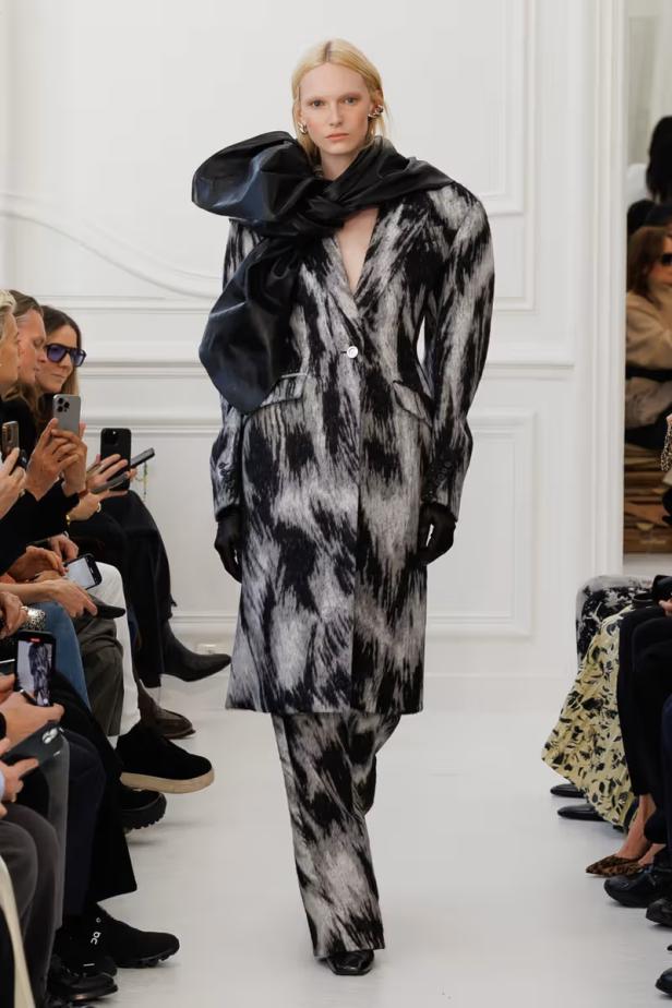 Ein Model präsentiert einen Hosenanzug mit großem, schwarzem Kragen auf dem Laufsteg.