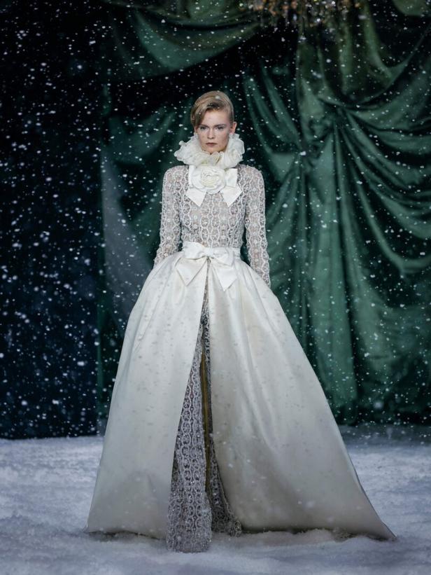 Eine Frau in einem weißen Kleid mit Rüschenkragen und Schleife steht im Schnee.