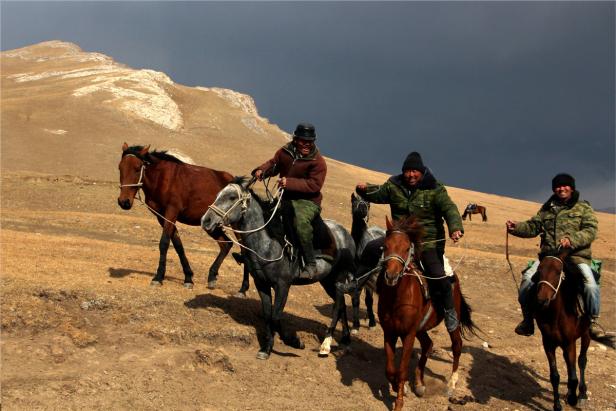 Eine Gruppe von Reitern führt ihre Pferde durch eine hügelige Landschaft.