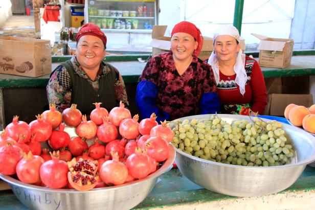 Drei Frauen verkaufen Granatäpfel und grüne Trauben auf einem Markt.