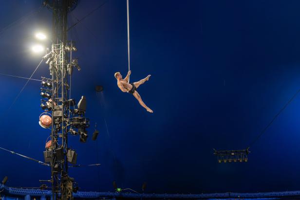 Ein Mann turnt an einem hängenden Seil vor einem blauen Hintergrund in einem Zirkus.