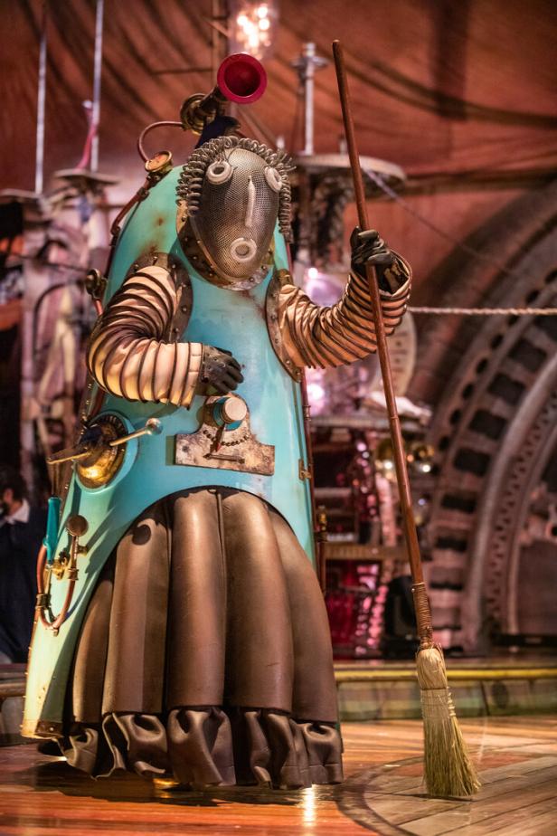 Eine skurrile, steampunk-artige Figur mit einem Besen auf einer Bühne.