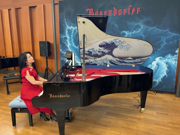 Eine Frau in einem roten Kleid spielt auf einem schwarzen Bösendorfer-Flügel mit Wellenmuster.