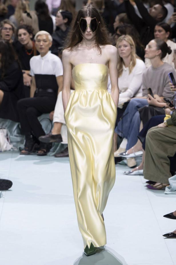 Ein Model in einem gelben, trägerlosen Kleid und futuristischer Sonnenbrille auf dem Laufsteg.