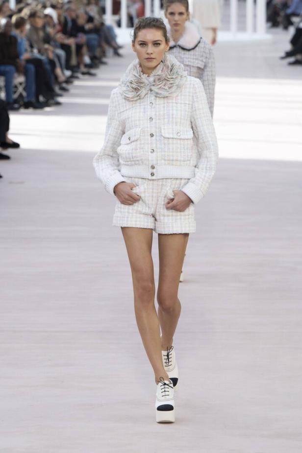 Ein Model präsentiert ein Tweed-Ensemble mit floralem Kragen und Plateauschuhen auf dem Laufsteg.