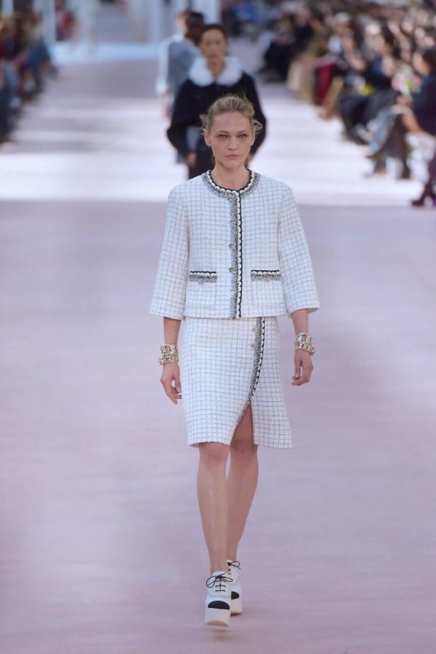 Ein Model in einem weißen Tweed-Kostüm mit passenden Plateauschuhen auf dem Laufsteg.