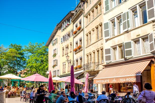 Ein belebtes Straßencafé mit Gästen vor historischen Gebäuden an einem sonnigen Tag.