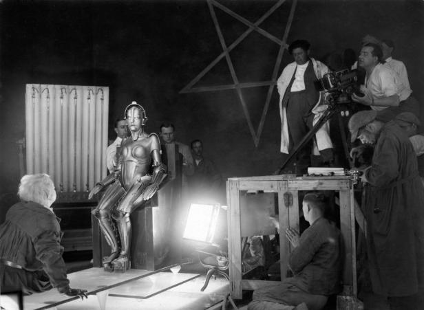 Der Roboter aus Metropolis sitzt, rundherum stehen Mitarbeiter am Filmset.