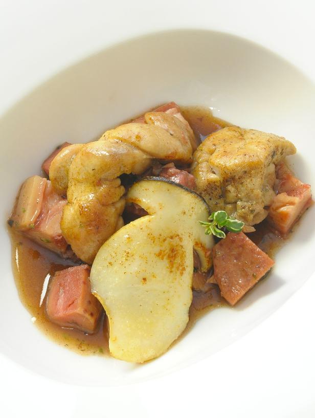 Ein Teller mit geschmortem Kaninchen, Pilzen und Speckwürfeln in Soße.