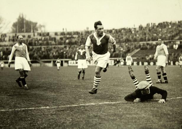 Ein Fußballspieler rennt mit dem Ball, während ein anderer zu fallen scheint.