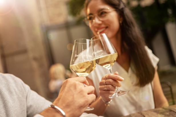 Zwei Weingläser, mit Weißwein, werden angestoßen.