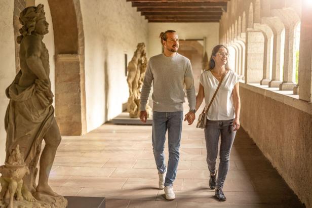 Ein Mann und eine Frau laufen Hand in Hand durch einen alten, lichtdurchfluteten Flur.