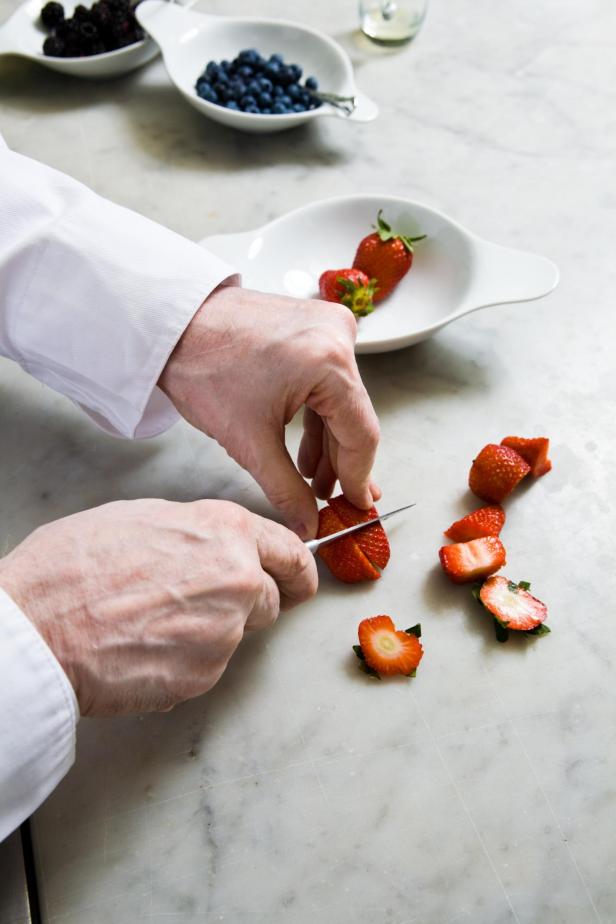 Ein Koch schneidet Erdbeeren für Crêpes mit Creme und frischen Früchten.