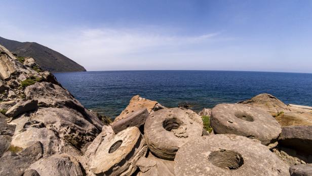 Ein Blick auf das Meer von einem felsigen Ufer mit alten Mühlsteinen.