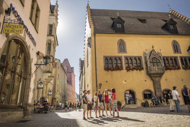 Eine Gruppe von Menschen steht auf einer gepflasterten Straße und unterhält sich in einer städtischen Umgebung.