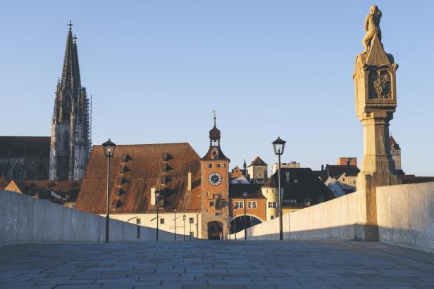 Blick auf Stadt mit Brücke, Uhrturm und Dom im Vordergrund, umgeben von städtischen Gebäuden.