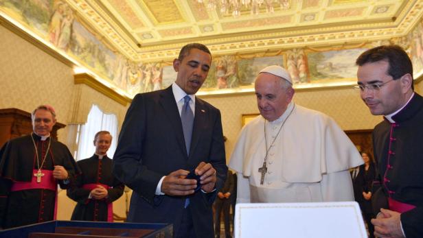 Barack Obama und Papst Franziskus betrachten gemeinsam ein Objekt in einem Raum des Vatikans.
