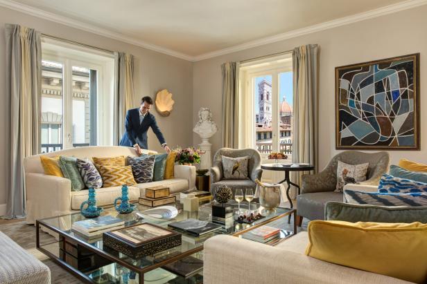 Ein Mann in einem Anzug arrangiert Kissen auf einem Sofa in einem luxuriösen Wohnzimmer mit Blick auf Florenz.