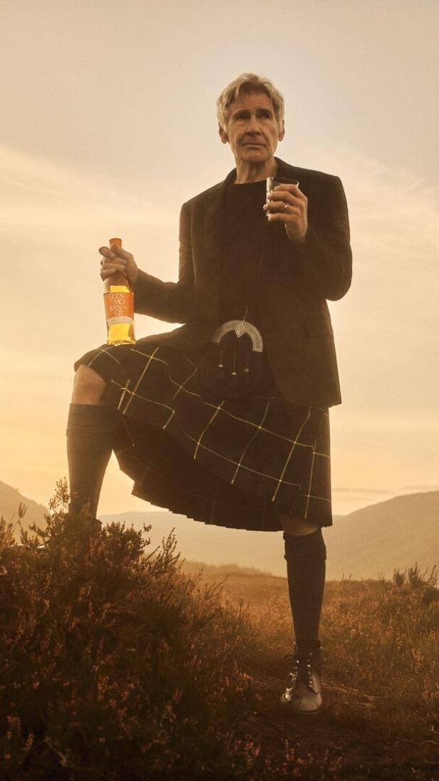Harrison Ford im Kilt, mit einer Flasche und einem Glas Glenmorangie Whisky in den schottischen Highlands.