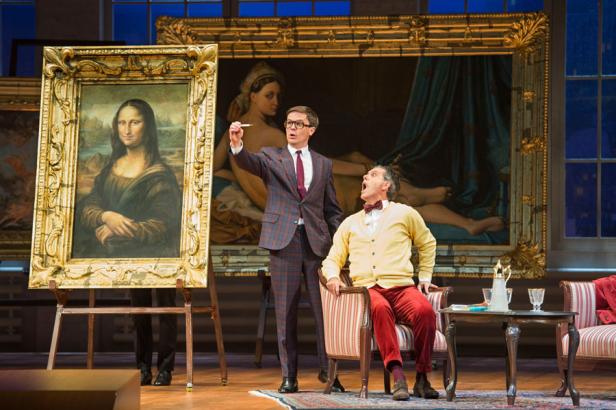 Auf einer Theaterbühne stehen zwei Männer vor Gemälden, darunter eine „Mona Lisa“-Darstellung.