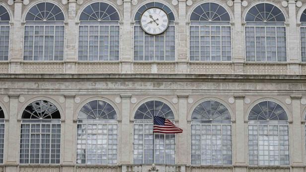 Die Fassade eines Gebäudes mit vielen Fenstern, einer Uhr und einer amerikanischen Flagge.