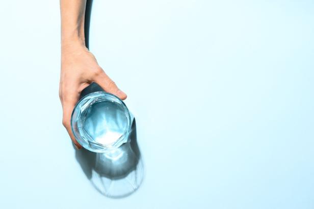 Eine Hand hält ein Glas Wasser auf einem hellblauen Hintergrund.