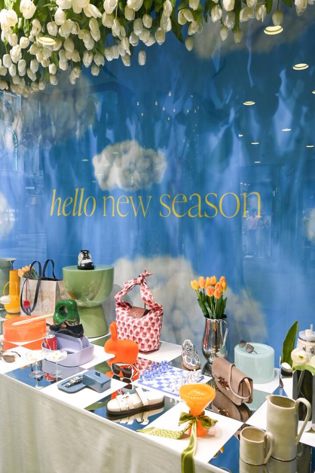 Ein Schaufenster mit dem Schriftzug „Hello New Season“ und verschiedenen Modeartikeln auf einem Schachbrettmuster.