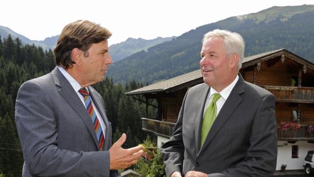 Zwei Männer in Anzügen unterhalten sich vor einer Bergkulisse.