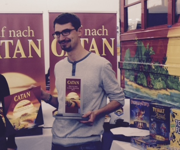Ein Mann mit Brille präsentiert die Spiele „Catan“ und „Tumult Royal“.