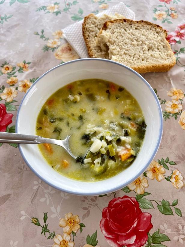 Eine Schüssel Gemüsesuppe mit Brot auf einem Tisch mit Blumenmuster.