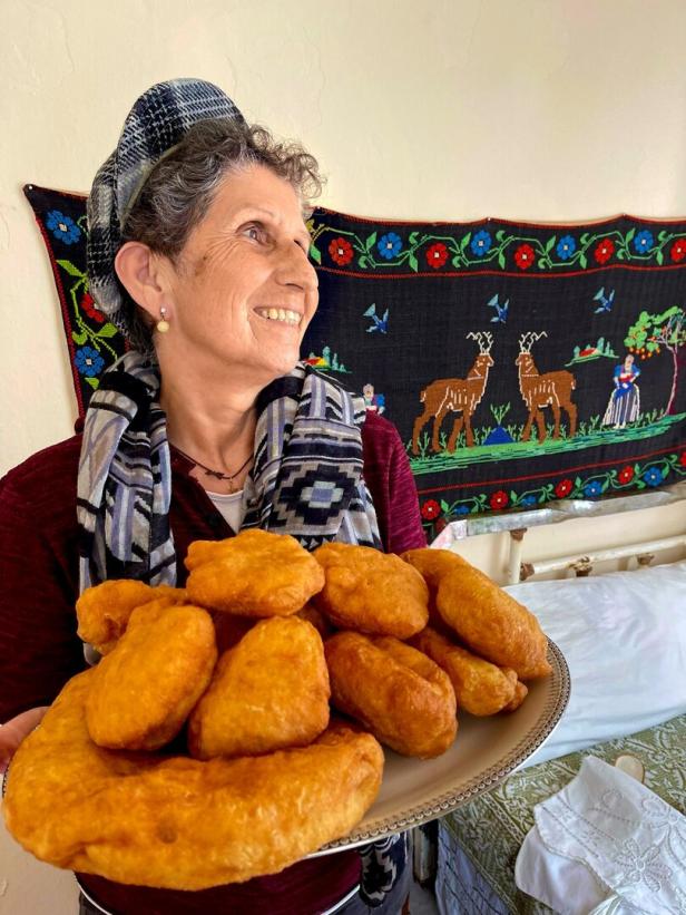 Eine lächelnde Frau präsentiert einen Teller mit frittiertem Teiggebäck.