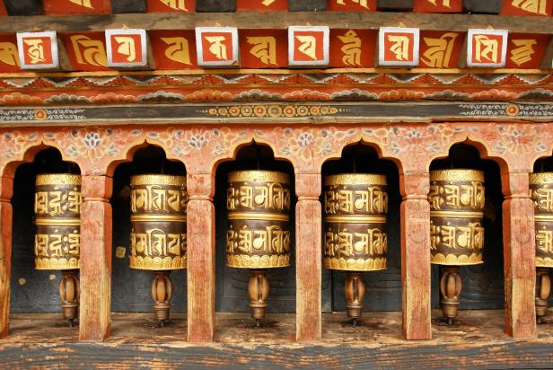 Mehrere Gebetsmühlen mit goldenen Inschriften in einem buddhistischen Tempel.