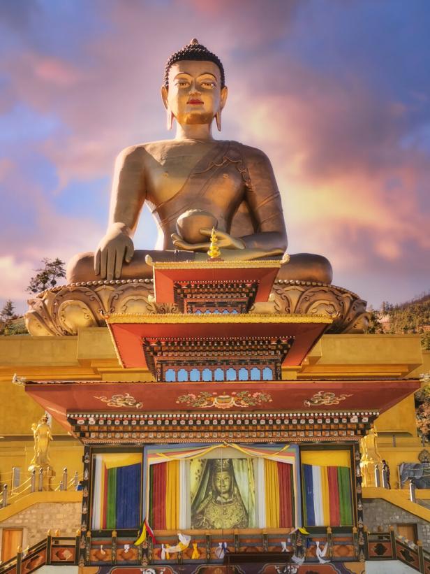 Eine große Buddha-Statue sitzt auf einem verzierten Gebäude unter einem bewölkten Himmel.
