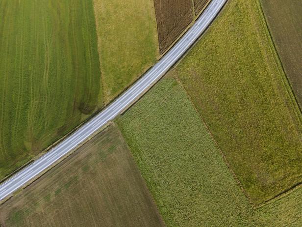 Eine Straße durchquert aus der Vogelperspektive eine Landschaft mit Feldern.