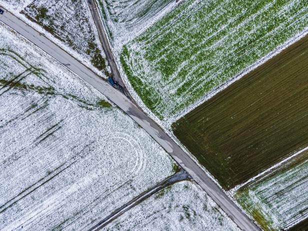 Luftaufnahme von Feldern mit leichten Schneefall und einer Straße.