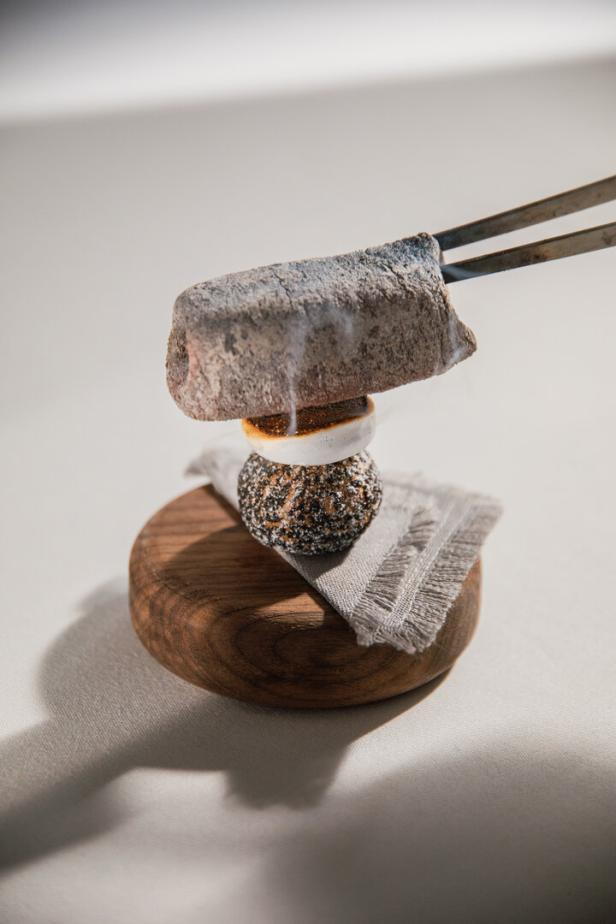 Ein Marshmallow wird mit einer glühenden Kohle und einer Zange geröstet.