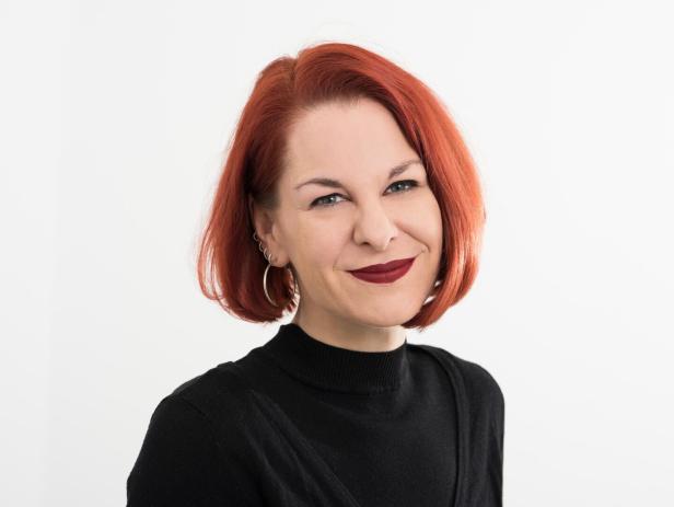 Eine Frau mit roten Haaren und dunklem Lippenstift lächelt.