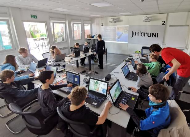 Eine Gruppe Kinder sitzt an Laptops in einem Raum der Junior Uni und lernt Programmieren.