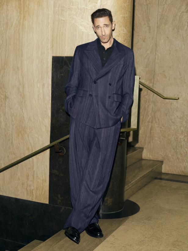 Adrien Brody posiert in einem blauen Anzug an einer Treppe.