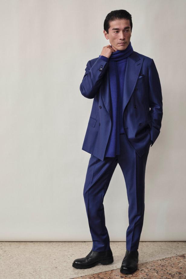 Ein Mann in einem blauen Anzug mit Rollkragenpullover und schwarzen Stiefeln posiert.