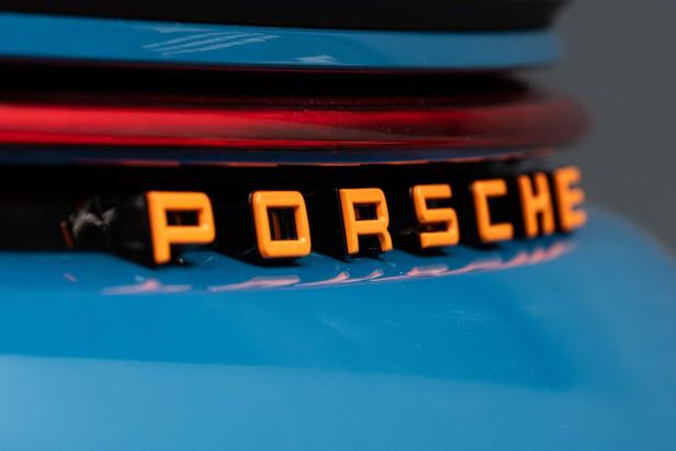 Der orangefarbene „Porsche“-Schriftzug auf einem blauen Auto.