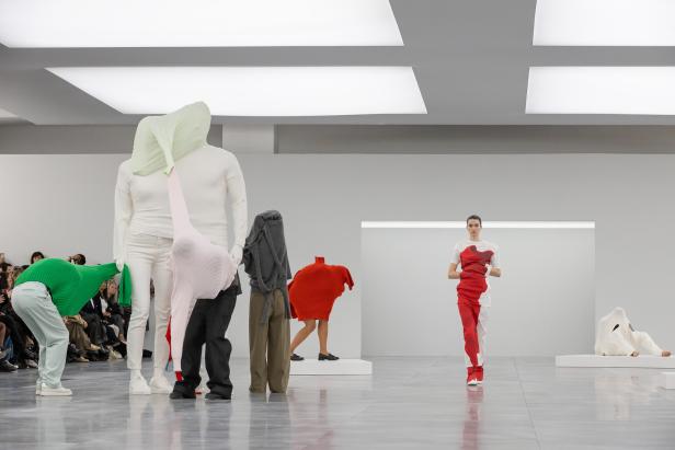 Eine Modenschau mit Models und skulpturartigen Kleidungsstücken in einem minimalistischen Raum.
