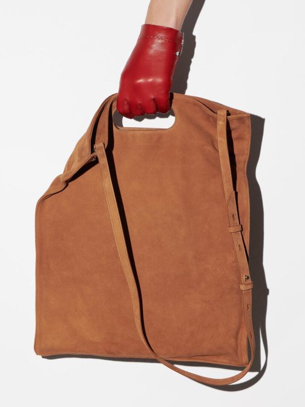 Eine Hand mit rotem Lederhandschuh hält eine große, braune Wildledertasche.