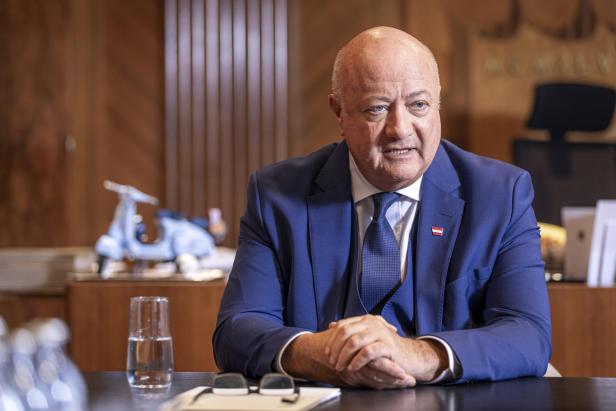 Christian Stocker sitzt an einem Tisch mit einer kleinen Vespa im Hintergrund.