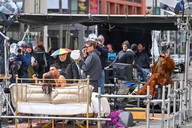 Ein Filmset mit Heidi Klum, die in einem braunen Pelzmantel und Stiefeln auf einem Stuhl sitzt.